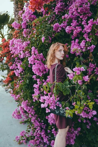 Portret van een mooie jonge vrouw die bij roze bloeiende planten staat