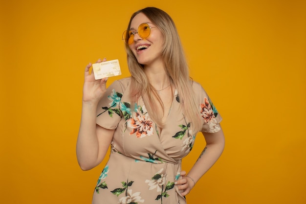 Portret van een mooie jonge vrouw die creditcard toont die over gele achtergrond wordt geïsoleerd