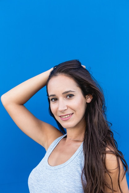 Portret van een mooie jonge vrouw die en met een blauwe muur op de achtergrond glimlacht stelt