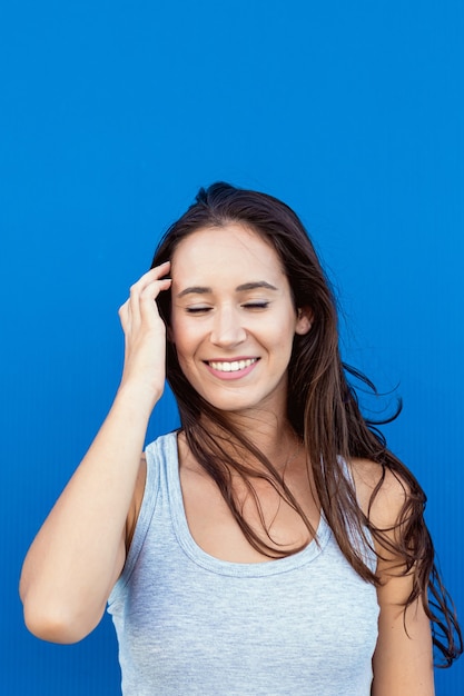 Portret van een mooie jonge vrouw die en met haar haar en de wind met een blauwe achtergrond glimlacht speelt