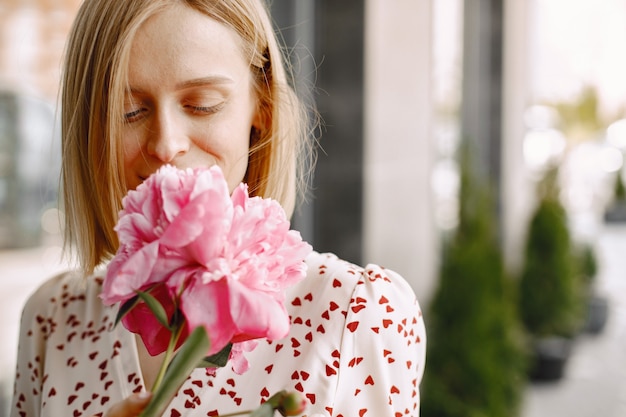 Portret van een mooie jonge vrouw die in de buurt van café buiten staat en een boeket bloemen vasthoudt. Vrouw met bril en jurk