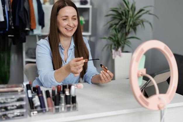 Foto portret van een mooie jonge vrouw die make-up maakt, in de spiegel kijkt en cosmetische cosmetica toepast