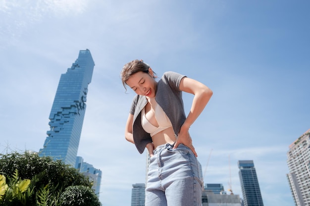 Portret van een mooie jonge vrouw die ontspant met uitzicht op de stad in een witte bikini en een spijkerbroek met lange benen