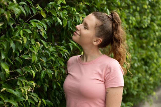 Portret van een mooie jonge vrouw die op een klimopmuur staat of in het groen glimlacht en wegkijkt