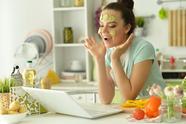 Foto portret van een mooie jonge vrouw die salade maakt en thuis een laptop gebruikt