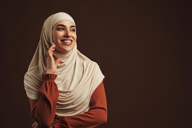 Portret van een mooie jonge vrouw in een beige hijab op een donkerbruine achtergrondKopieer de ruimte