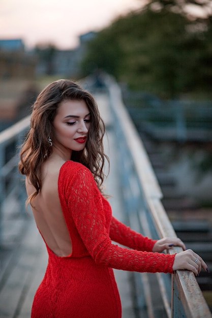 Portret van een mooie jonge vrouw in een lange rode jurk staat op de brug