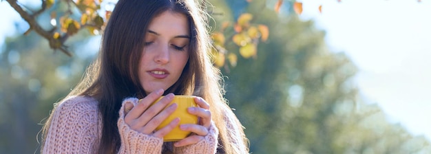 Portret van een mooie jonge vrouw in een stijlvolle gebreide trui die op een zonnige dag op het gouden herfstbos staat. Tijd om te ontspannen en wat koffie te drinken
