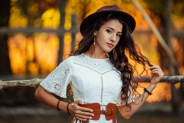 Portret van een mooie jonge vrouw in een witte jurk met overknee laarzen en een hoed met een riem en een pony op een rustieke boerderijstal