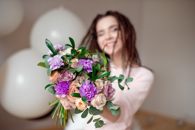 Portret van een mooie jonge vrouw in een zomerjurk en een strooien hoed houdt een anjer, rozen boeket en kijkt over haar schouder