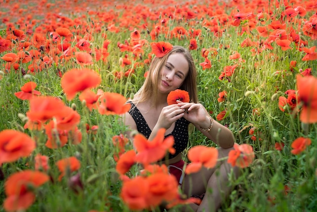 Portret van een mooie jonge vrouw in sportkleding zittend op bloeiende papavers veld