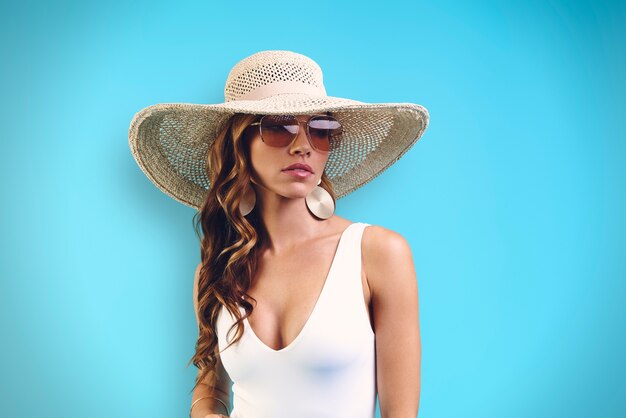 Portret van een mooie jonge vrouw met een elegante hoed die wegkijkt terwijl ze tegen een blauwe achtergrond staat
