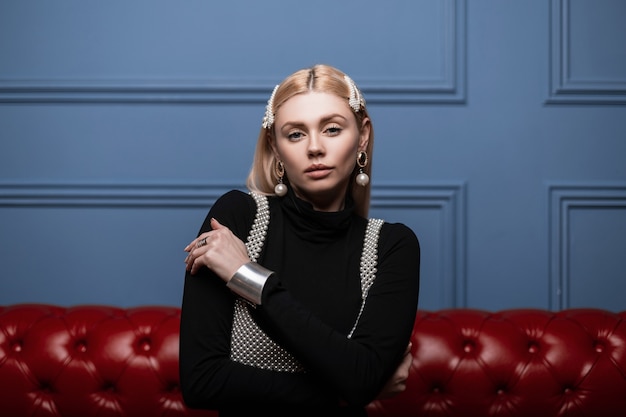 Portret van een mooie jonge vrouw met natuurlijke make-up in een chique parel top in een zwart shirt met vintage haarspelden in de studio op een rode leerbank