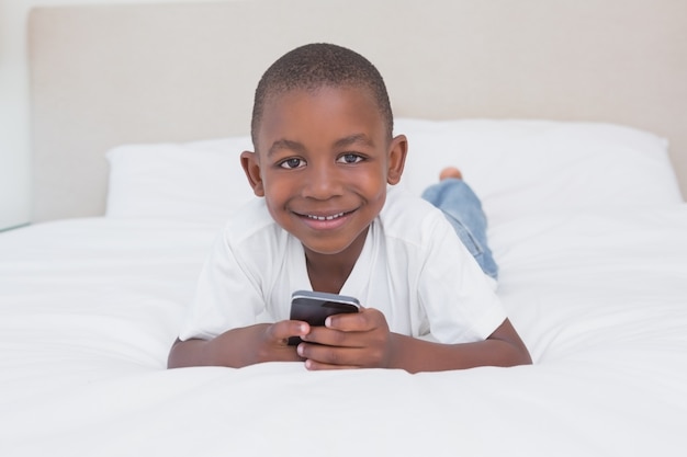 Portret van een mooie kleine jongen met behulp van smartphone in bed