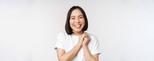 Portret van een mooie Koreaanse vrouw met een gezonde witte glimlach die lacht en gelukkig kijkt naar de camera die in een t-shirt staat over een witte studioachtergrond