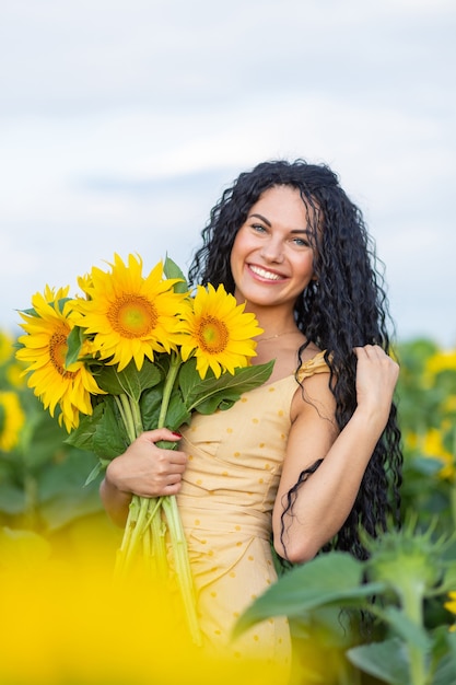 Portret van een mooie lachende donkerharige vrouw met een boeket zonnebloemen