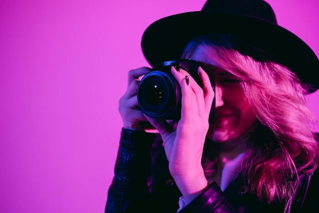 Portret van een mooie meisjesfotograaf met een hoed die foto's maakt in de studio op een fioletachtergrond