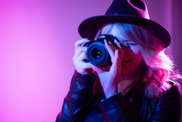 Portret van een mooie meisjesfotograaf met een hoed die foto's maakt in de studio op een fioletachtergrond