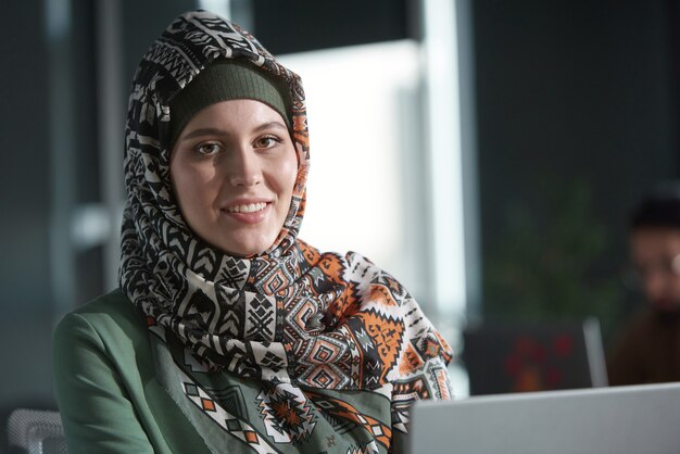 Portret van een mooie moslimvrouw in hijab die naar de camera glimlacht terwijl ze op kantoor zit