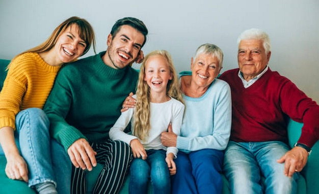 Portret van een mooie multi-generatie familie die thuis op de bank zit en naar de camera kijkt