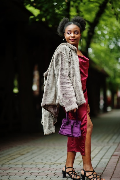 Portret van een mooie natuurlijke jonge Afrikaanse vrouw met afrohaar. Zwart model in rode zijden jurk.