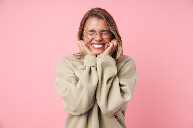 Portret van een mooie opgewonden vrouw in een bril die lacht met gesloten ogen geïsoleerd op roze