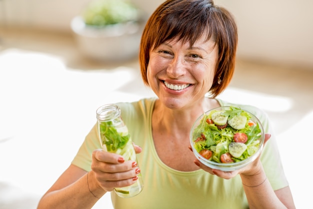 Portret van een mooie oudere vrouw in groen t-shirt met een salade binnen