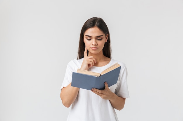 Portret van een mooie peinzende jonge vrouw casual gekleed staande geïsoleerd op wit, een boek lezen
