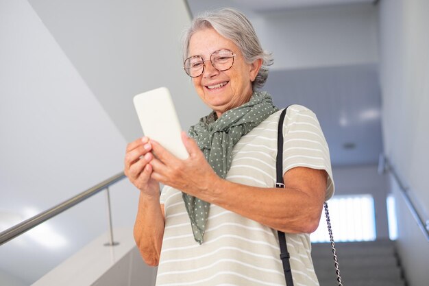 Portret van een mooie senior blanke vrouw die de trap afloopt in een gebouw met behulp van een mobiele telefoon Lachende volwassen vrouw houdt de telefoon in de hand