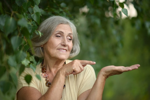 Portret van een mooie senior vrouw in groen park wijzend op lege copyspace