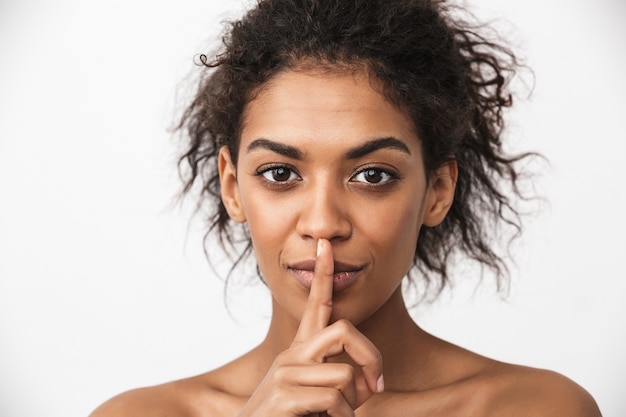 portret van een mooie serieuze jonge Afrikaanse vrouw poseren geïsoleerd over witte muur met stilte gebaar.