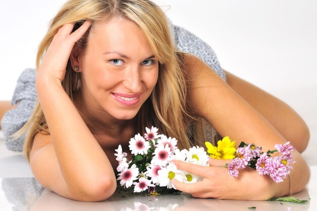 Portret van een mooie sexy jonge blonde vrouw poseren in studio in een mini-jurk met bloemen op een witte scène