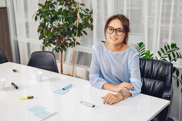 Portret van een mooie slanke mooie vrouw die op kantoor werkt en aan een witte tafel zit tegen een achtergrond van bloemen en ramen. baan concept