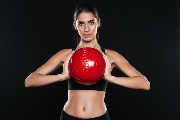 Portret van een mooie sportvrouw die een fitnessbal vasthoudt en naar de voorkant kijkt over een zwarte muur