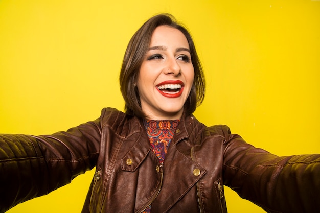 Portret van een mooie succesvolle glimlachende vrouw die selfie op een gele muur doet