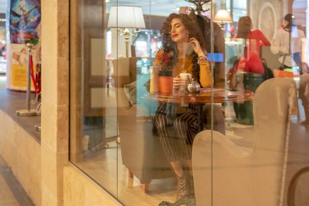 portret van een mooie tevreden vrouw aan een tafel in een café achter glas