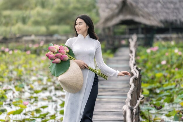 Portret van een mooie Vietnamese vrouw met een traditionele Vietnamese hoed die de roze lotus vasthoudt