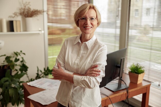 Portret van een mooie volwassen vrouw freelancer in een bril op de achtergrond van een kantoor thuis