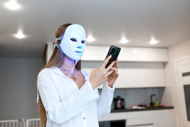 Portret van een mooie vrouw die aan de telefoon communiceert en een lichttherapie-gezichtsmasker uitvoert