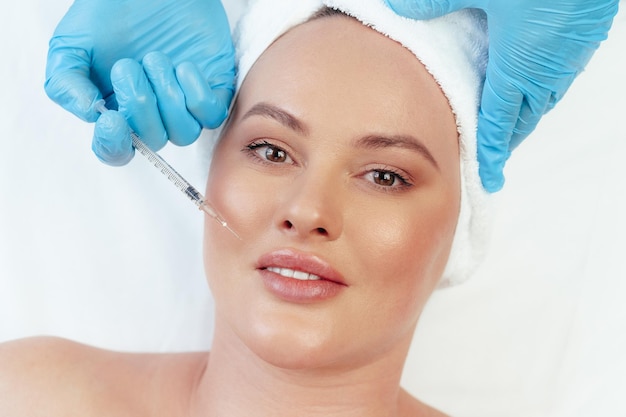 Portret van een mooie vrouw die een injectie met botox in haar gezicht krijgt