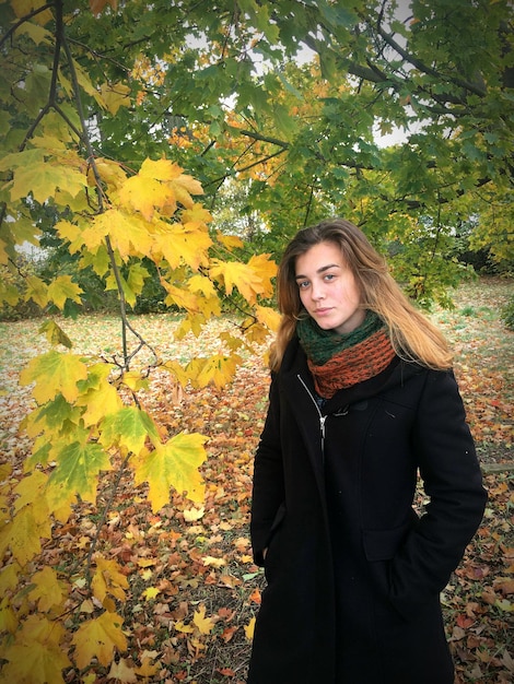 Portret van een mooie vrouw die in de herfst bij een boom staat