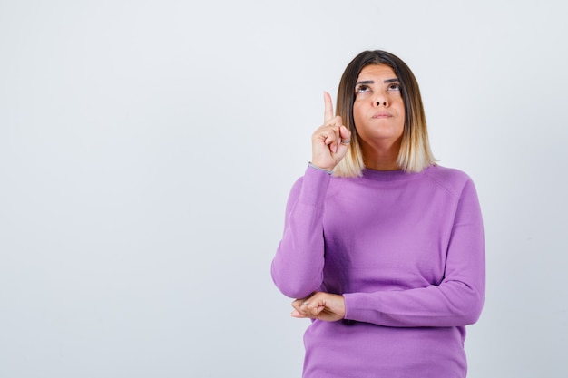 Portret van een mooie vrouw die naar boven wijst, omhoog kijkt in een paarse trui en er gefocust vooraanzicht uitziet