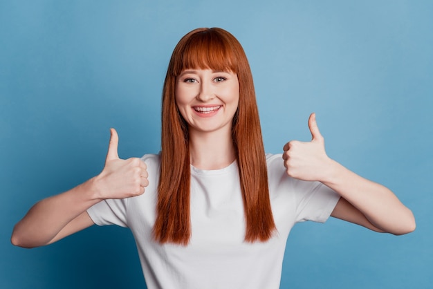 Portret van een mooie vrouw die twee duimen op een blauwe achtergrond toont