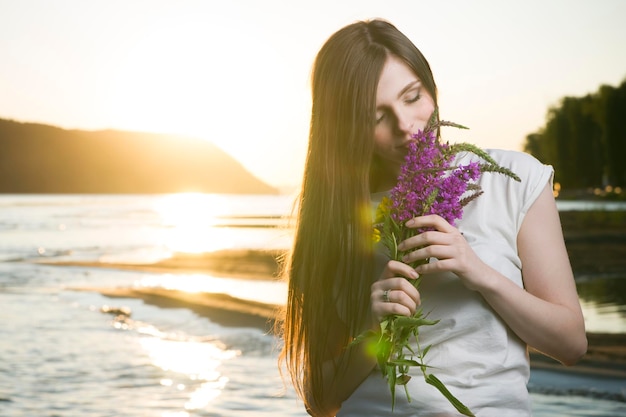 Portret van een mooie vrouw in een hoed op een achtergrond van een zonsondergang. Meisje met een boeket bloemen