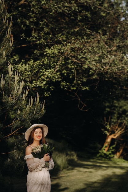 Portret van een mooie vrouw in een witte jurk en een hoed met lelies van de vallei Een meisje in de natuur Lentebloemen