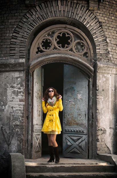 Portret van een mooie vrouw in gele overjas en zonnebril die op zonnige lentedag door de oude stad loopt