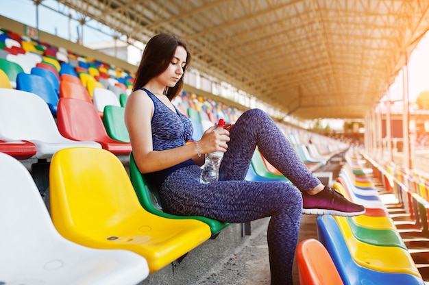 Portret van een mooie vrouw in sportkleding zitten en drinkwater in het stadion.