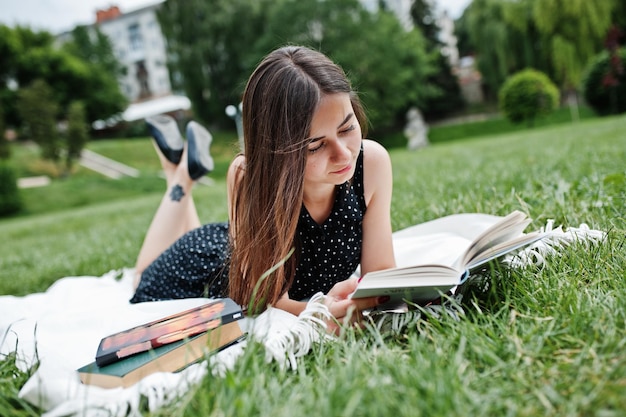 Portret van een mooie vrouw in zwarte polka dot-jurk die op de deken op het gras ligt en leest