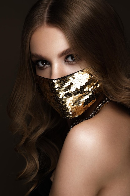 Portret van een mooie vrouw met een gouden masker met pailletten en klassieke make-up Maskermodus tijdens de covid-pandemie