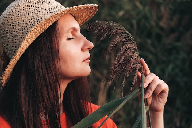 Portret van een mooie vrouw met een strohoed en gekleed in rode kleren op een achtergrond van riet